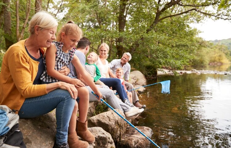 Multi-generational family relaxes by the water and collects rocks - just one of many family staycation ideas for summer fun.